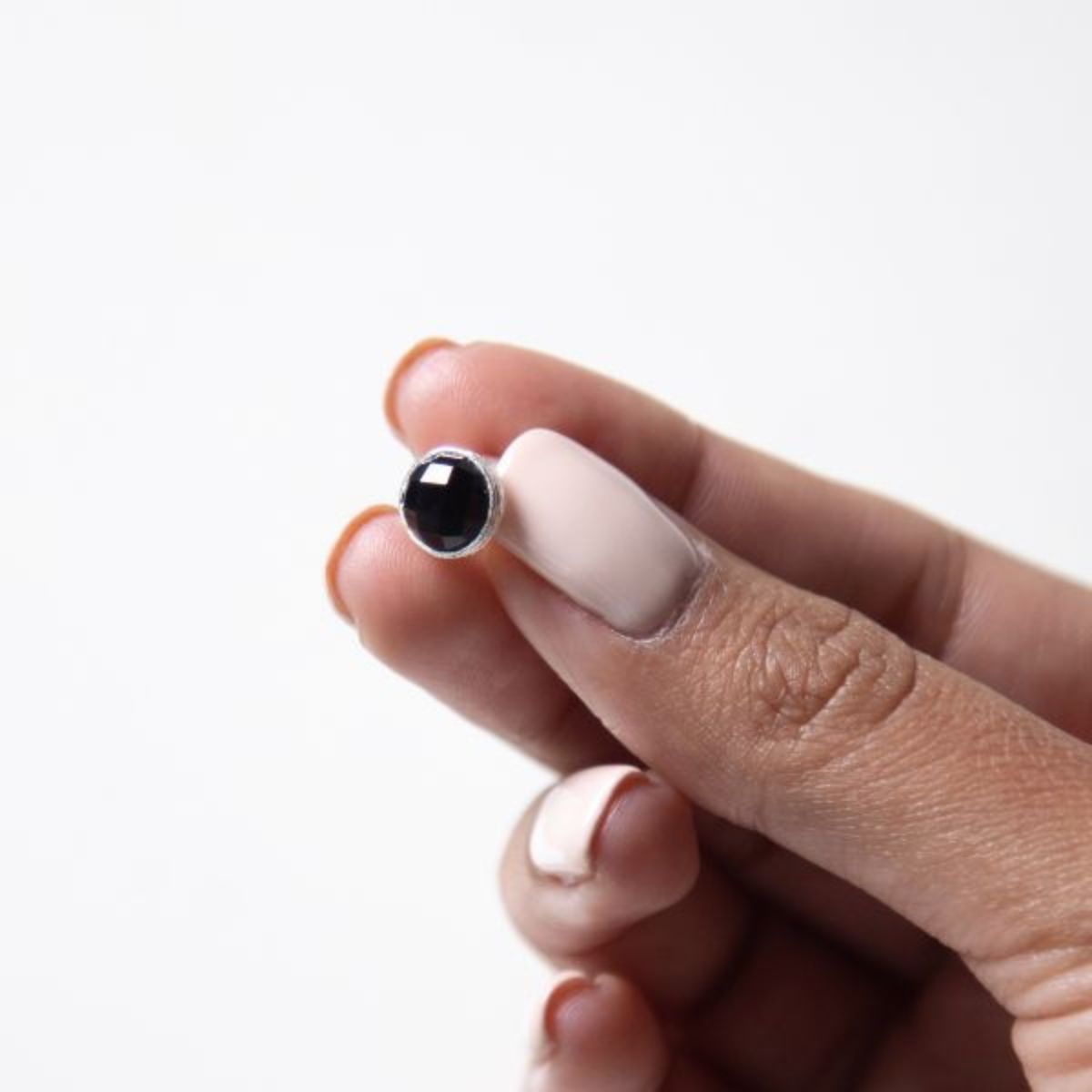a woman holding a black onyx stud in her fingers